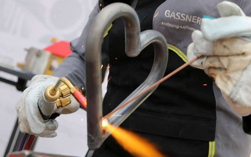 Image. Trainee welds a heart out of pipes at the trainee fair.
